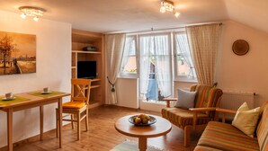 Ein gemütliches Wohnzimmer mit einem Holztisch, einer Couch, einem Fernseher und einem Fenster mit Vorhängen.
