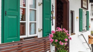 Ein Gebäude mit grünen Fensterläden, einer Holzbank und einem Blumentopf mit rosa Blüten.