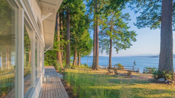 Una terraza de madera que conduce a una zona de playa con vistas al océano y a árboles altos.