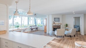 Una cocina amplia con una isla grande, pisos de madera e iluminación colgante. Cuenta con un comedor con un banco y sillas, además de una chimenea con repisa.