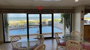 Une table en verre avec des chaises en osier, une vue sur une piscine et une plage, et un panneau de sortie au plafond.