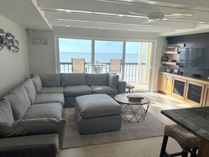 Un salon moderne avec un canapé d’angle gris, une table basse ronde et un coin repas comprenant une table sombre et des chaises en osier.