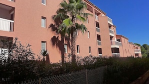 Un edificio de varios pisos con balcones, una palmera y una cerca de malla metálica.