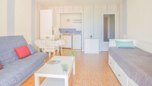 Un espacio habitable compacto con sofá, cama, una pequeña mesa de comedor y kitchenette.