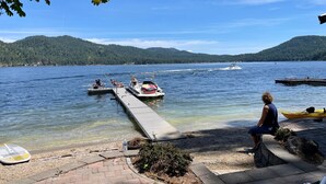 Une jetée au bord d’un lac, avec des bateaux, un kayak et une personne assise sur un banc.