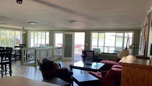 Une pièce spacieuse comprenant un coin repas, un coin salon avec un canapé et des fauteuils, et de grandes fenêtres donnant sur l’extérieur.