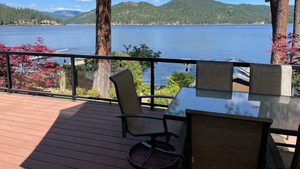 Une terrasse dotée d’une table et de chaises en verre, offrant une vue sur un lac et sur des montagnes qui se dessinent à l’horizon.