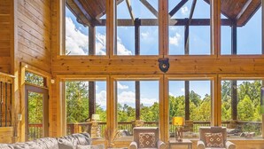A spacious wooden cabin with large windows, a stone fireplace, and a television. - Secluded 4BRMountain Retreat:Stunning Views, Pool Table, Arcade, HotTub, FirePit (Sevierville)