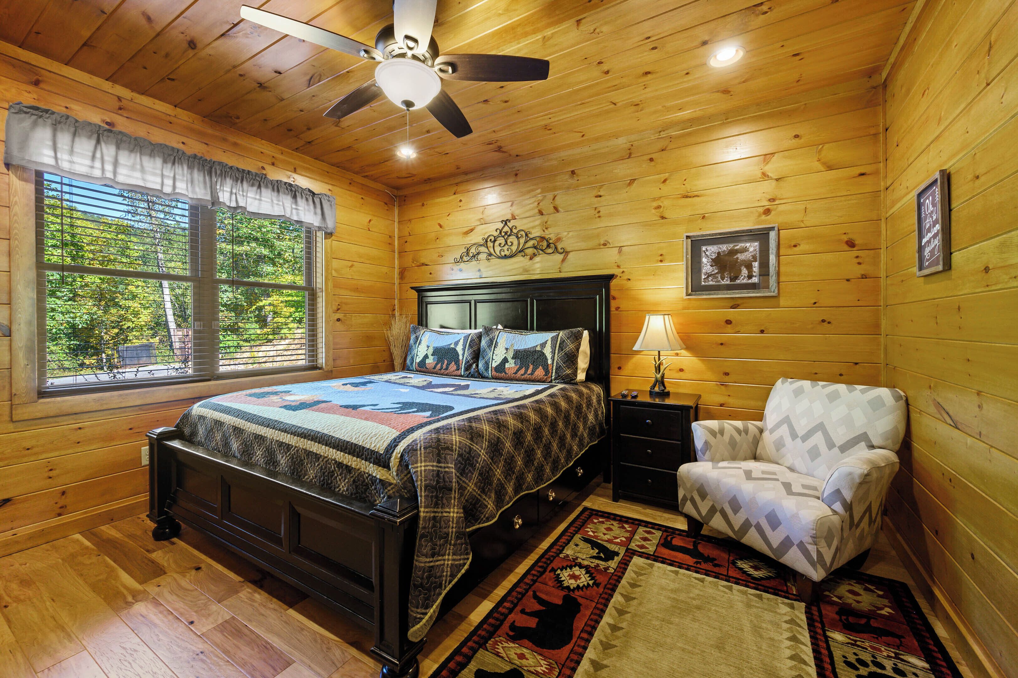 Een slaapkamer in een houten chalet met een bed, nachtkastje, stoel en plafondventilator.