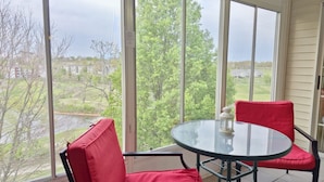 Une véranda avec une table en verre et des chaises rouges, de grandes fenêtres donnant sur un paysage verdoyant.