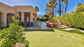 Un área de piscina con patio, mobiliario exterior y palmeras.