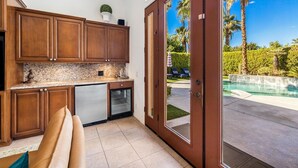 Cocina con armarios de madera, encimera de granito y vistas a una piscina y palmeras.