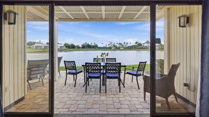 A patio with a table and chairs, a view of a lake, and a building in the background. - Lakeside Sunset Retreat | Ground Floor | 3 En Suites | Optional Saddlebrook Resort Amenities (Wesley Chapel)