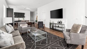 Una sala de estar moderna con una mesa de centro de vidrio, sofás grises y un televisor negro en la pared.