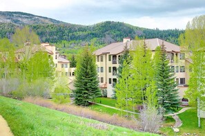 A multi-story residential building with a symmetrical facade, surrounded by lush greenery and a hilly backdrop.