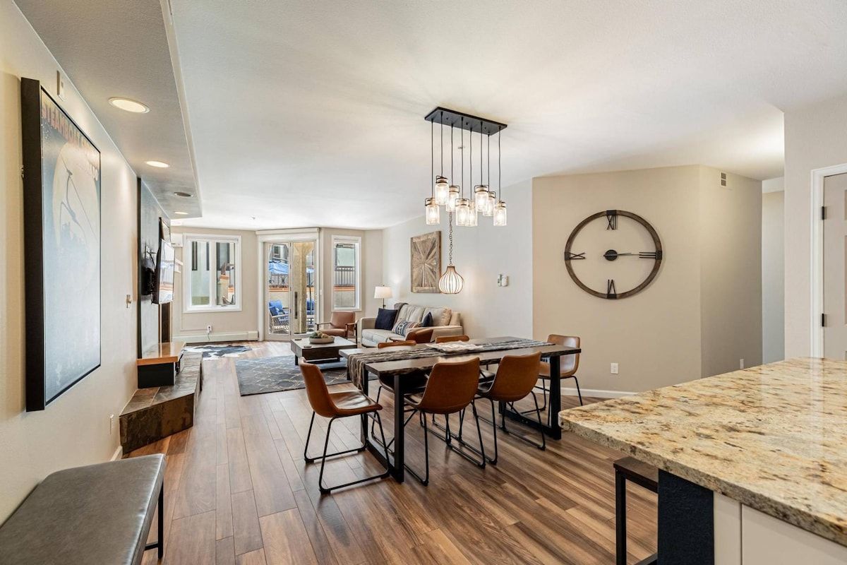 Une cuisine moderne dotée d’un grand îlot central, d’un plancher en bois et d’un coin repas avec des chaises et une table.