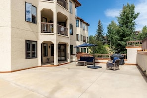 Un immeuble à plusieurs étages doté d’un patio couvert, aménagé avec du mobilier d’extérieur et un barbecue.