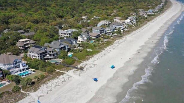 An aerial view of a coastal residential area with houses along the beach, a clear sky, and a calm sea. - Beach. View. Suite. 1 br. 1 ba. Sleeps 5 (Hilton Head Island)