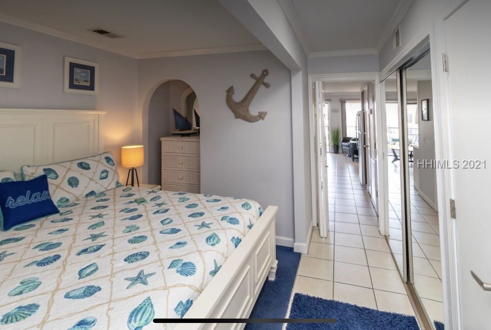A bedroom with a bed, a dresser, a wall-mounted anchor decoration, and a hallway leading to another room.