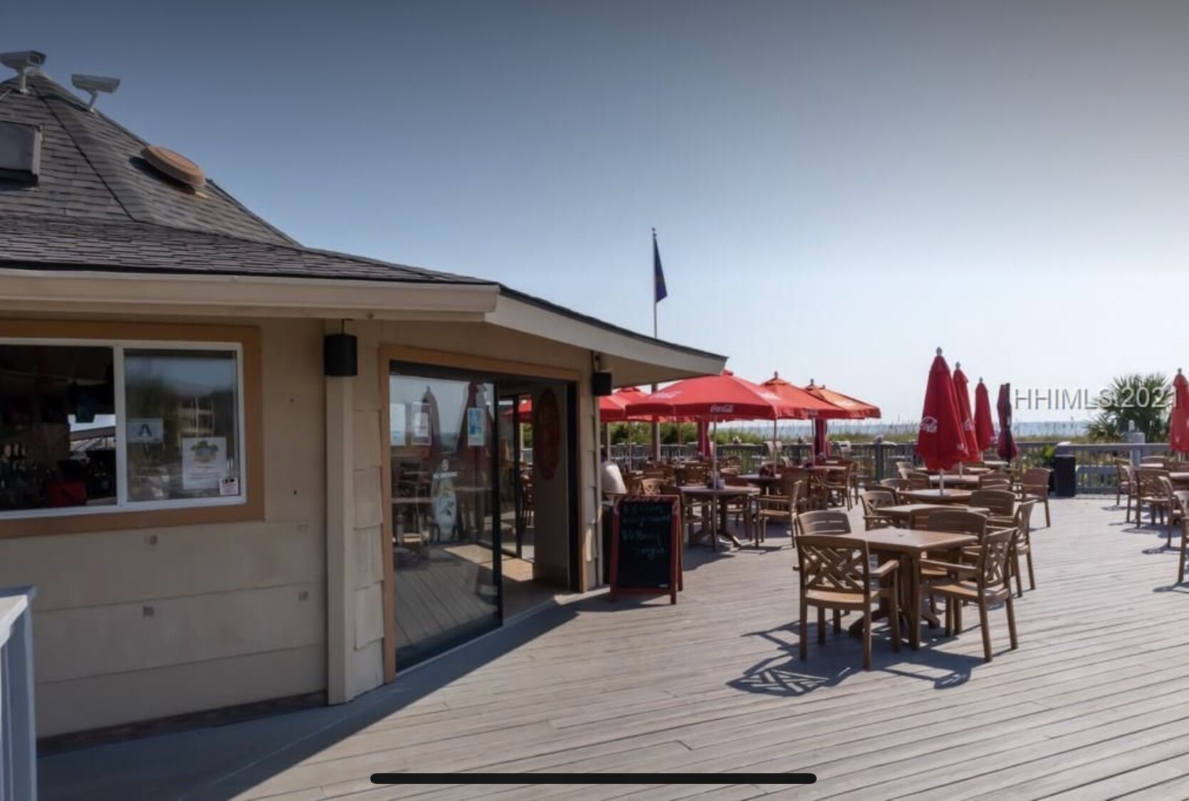 A seaside restaurant with outdoor seating and red umbrellas.