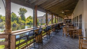 An outdoor deck with wooden flooring, metal chairs, and tables, overlooking a body of water and greenery. - Beach. View. Suite. 1 br. 1 ba. Sleeps 5 (Hilton Head Island)