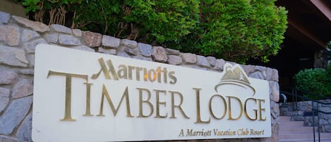 A sign for Marriott's Timber Lodge, a Marriott Vacation Club Resort, with a stone wall and greenery in the background.