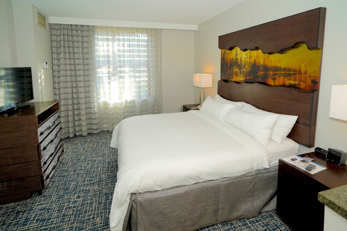 A hotel room with a large bed, a TV, a dresser, and a painting on the wall.