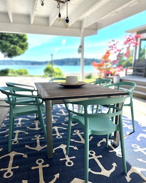 Relax in this serene outdoor seating area with a table and chairs, overlooking a tranquil body of water and lush greenery.