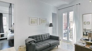 Ein modernes Wohnzimmer mit einem grauen Sofa, einem Holzschemel und einem kleinen Tisch mit einer Lampe.