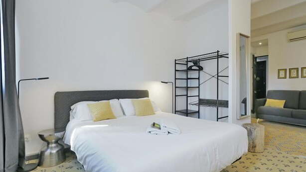 A hotel room with a bed, a bedside table, a lamp, a wardrobe, and a mirror. - Casa Nanit Apt B near Camp Nou (L'Hospitalet de Llobregat)