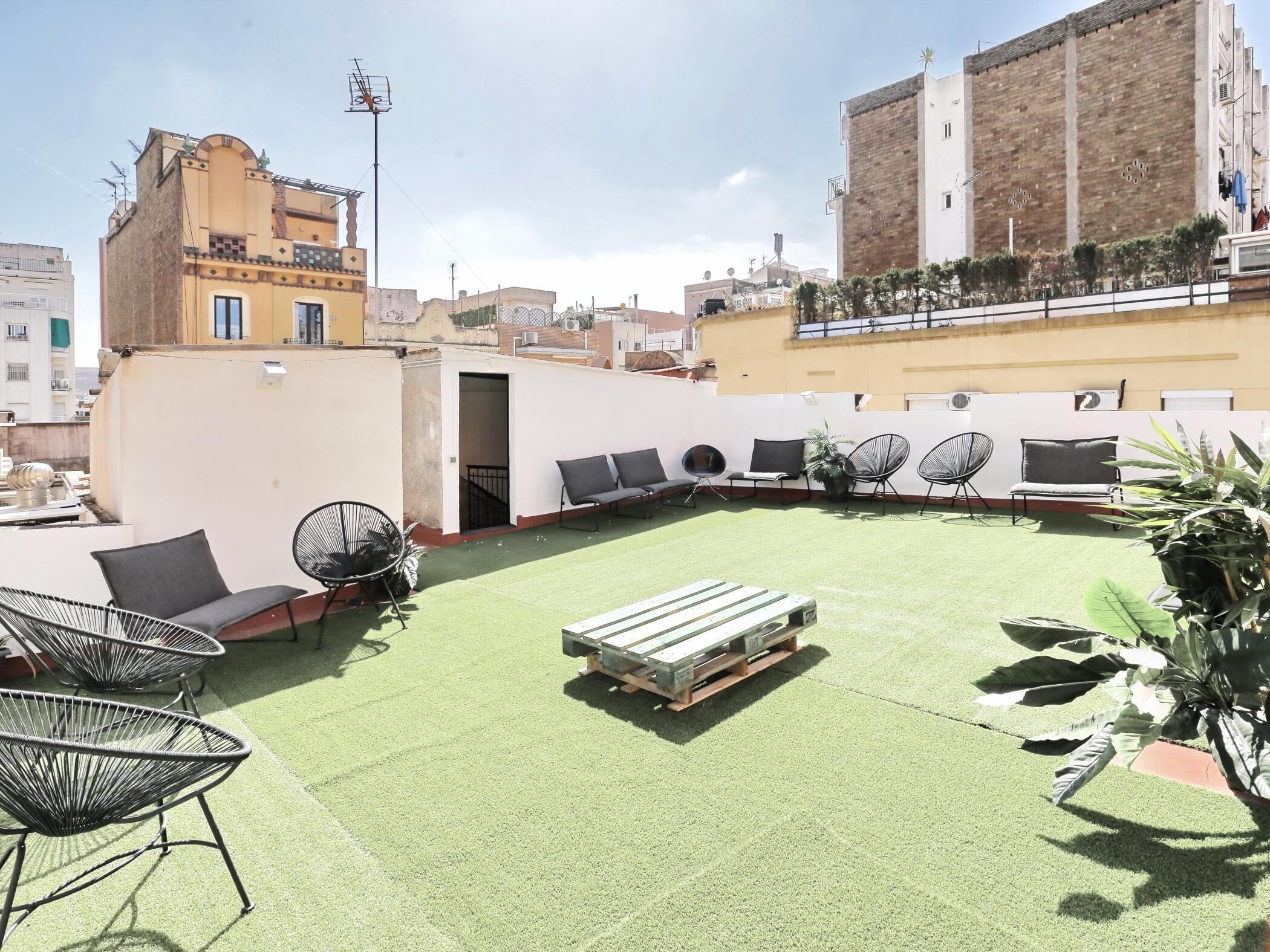 Una terraza en la azotea con césped artificial verde, sillas de estructura metálica negra y un banco de madera.
