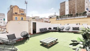 A rooftop terrace with green artificial turf, black wireframe chairs, and a wooden bench. - Casa Nanit Apt B near Camp Nou (L'Hospitalet de Llobregat)