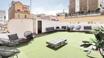 Una terraza en la azotea con césped artificial verde, sillas de estructura metálica negra y un banco de madera.