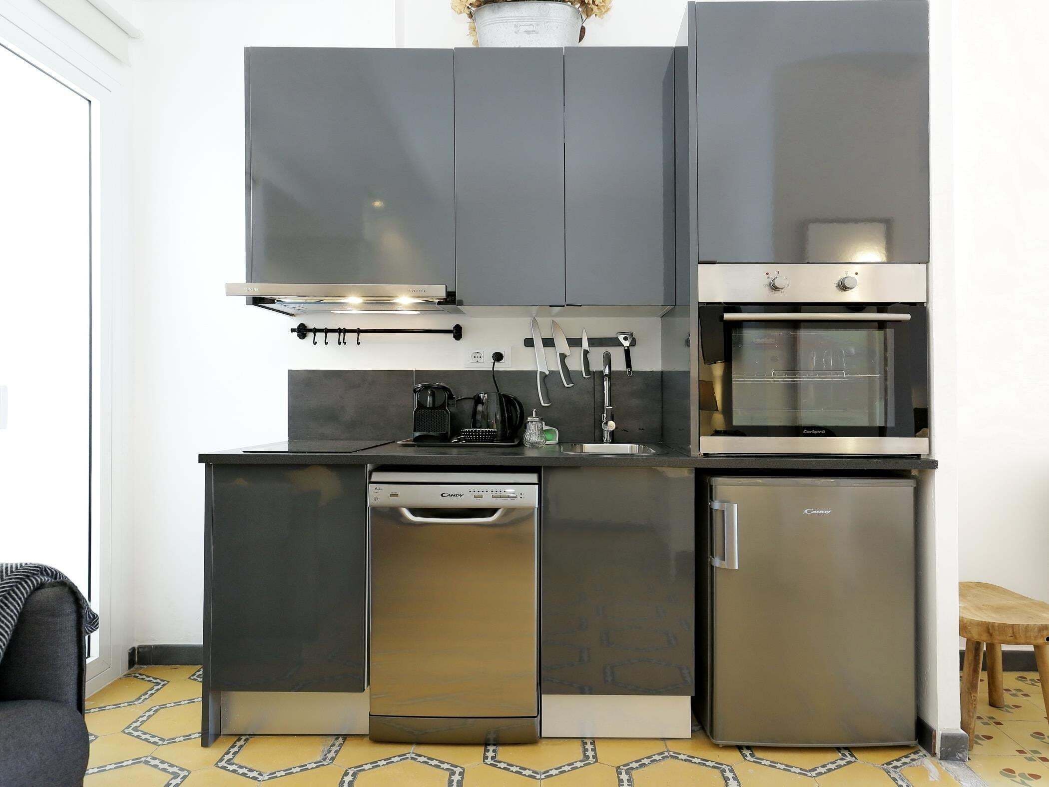 Cocina compacta con lavavajillas, horno y cafetera sobre la encimera.
