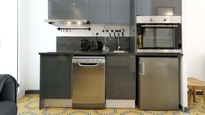 A compact kitchen with a dishwasher, oven, and a coffee maker on the countertop. - Casa Nanit Apt B near Camp Nou (L'Hospitalet de Llobregat)