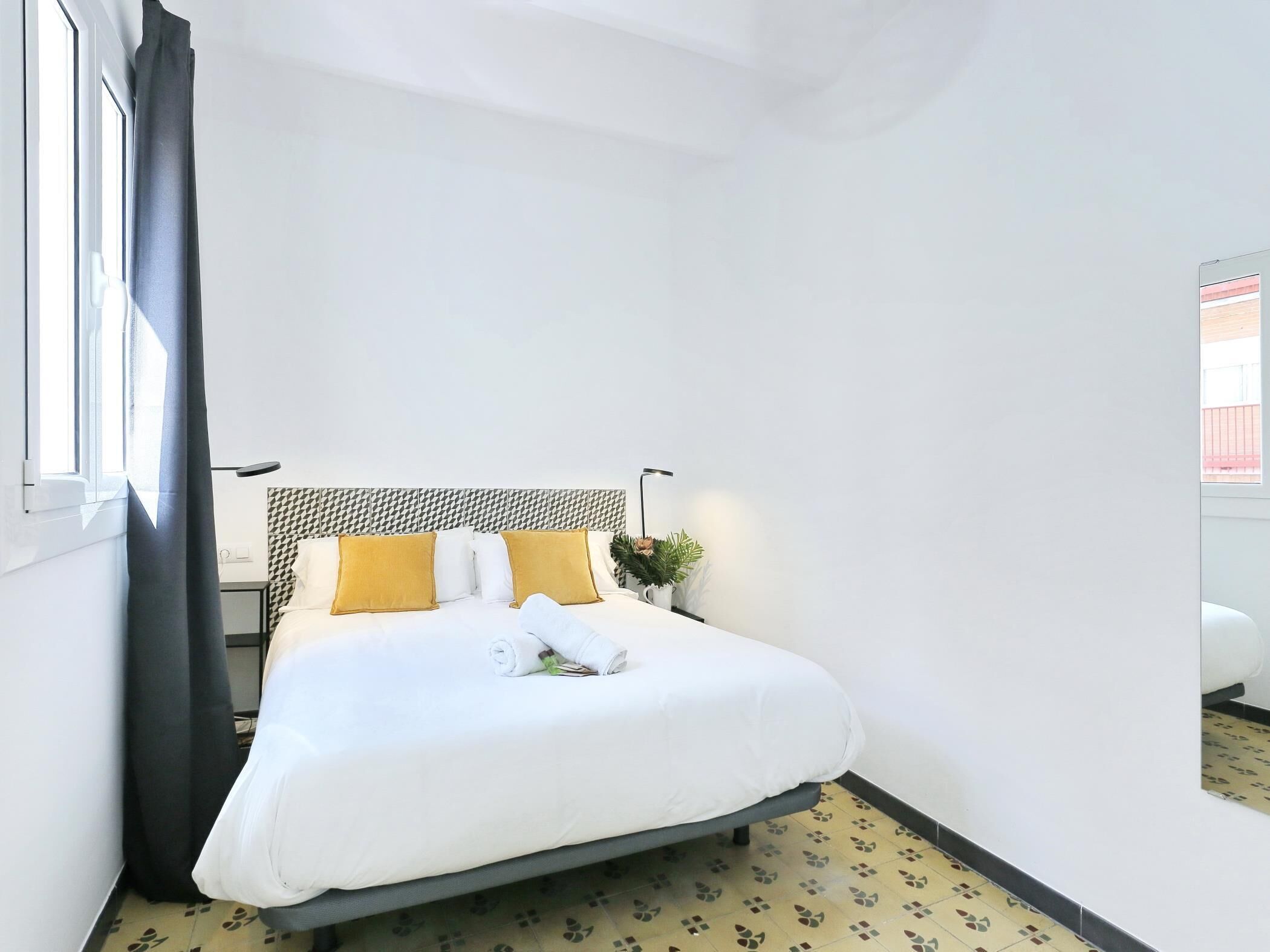 A hotel room with a bed, a headboard, a nightstand, a lamp, and a window with curtains.