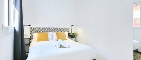 A hotel room with a bed, a headboard, a nightstand, a lamp, and a window with curtains.