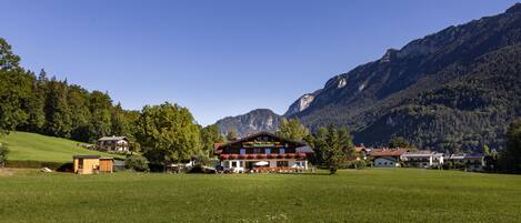 A mountain lodge with a large open field in front, surrounded by forested hills and mountains.