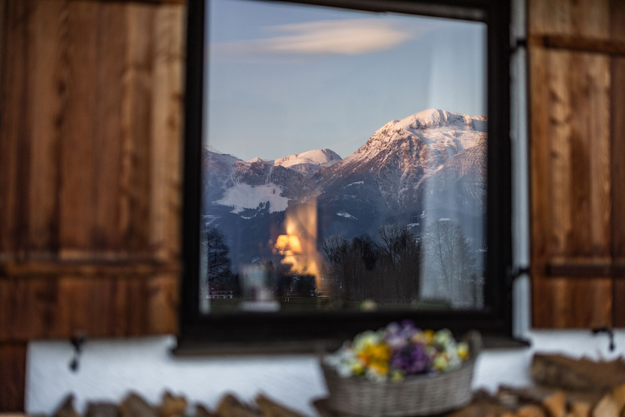 Une fenêtre donnant sur des montagnes enneigées et une source de lumière chaleureuse au loin.