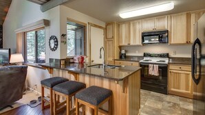 A modern kitchen with wooden cabinets, a granite countertop, a stainless steel refrigerator, and a built-in oven. - Sunriver Family Escape with 6 SHARC Passes (Sunriver)