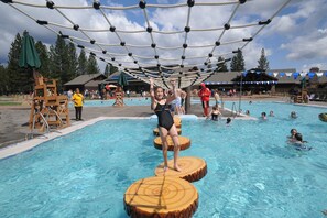 A swimming pool with wooden floating platforms and a rope net overhead.