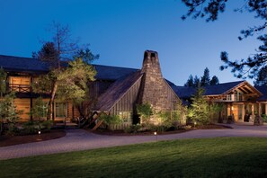 A rustic lodge with a prominent stone chimney, wooden exterior, and a well-maintained lawn.