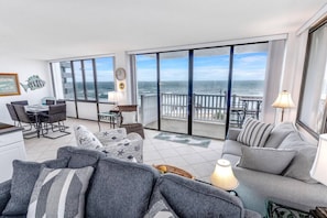 A spacious living area with a large balcony overlooking the ocean, featuring a dining table, seating area, and a view of the sea. - Ocean View 6th Floor Nautilus Condo with Wrap-Around Balcony & Pool | Tennis | Flagler Beach (Flagler Beach)