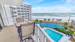 A balcony with a pool, chairs, and a view of the ocean and beach.