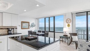 A modern kitchen with a large island, dining area with a view of the ocean, and a living area with a balcony overlooking the sea.