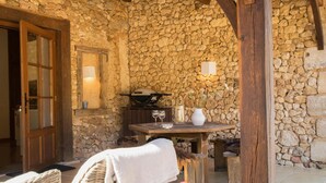 A stone-walled outdoor area with wicker furniture, a table with glasses, and a stone bench. - Charming villa with shared pool (Issac)
