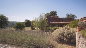 A rustic stone building with a tiled roof, surrounded by dense shrubbery and a wooden fence. - Charming villa with shared pool (Issac)