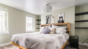 A bedroom with a bed, a bedside table, a lamp, and artwork on the wall.