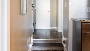 A hallway with a patterned rug, a door at the end, and a kitchen area with a countertop.