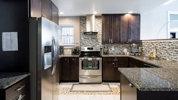 A modern kitchen with dark cabinetry, stainless steel appliances, a tiled backsplash, and granite countertops.